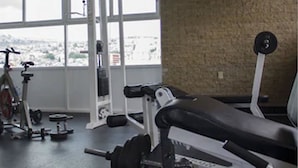 Un gimnasio con equipo de levantamiento de pesas, una banca y una bicicleta al fondo.