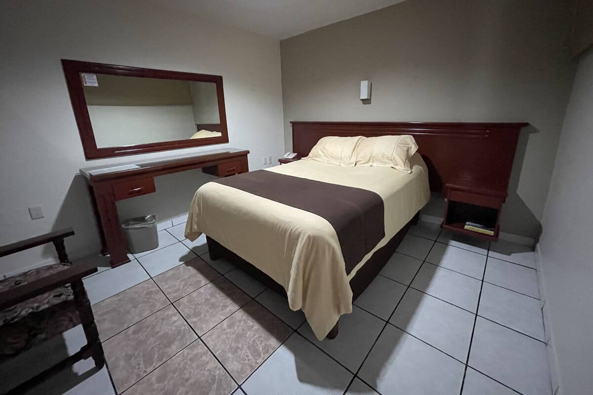 A bedroom with a bed, a desk, a mirror, and a nightstand.