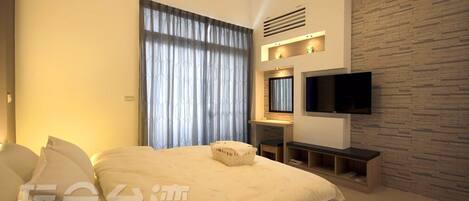 A modern hotel room with a large bed, a flat-screen TV mounted on the wall, and a stone-textured accent wall.