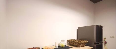 A kitchen with a refrigerator, a wooden countertop, a basket, and a bowl of food.