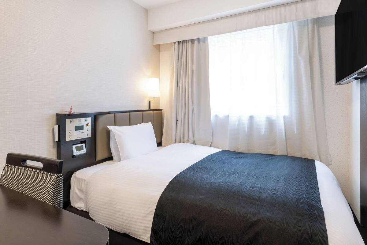 Une chambre d’hôtel avec un lit, un bureau, une télévision et une fenêtre avec des rideaux.