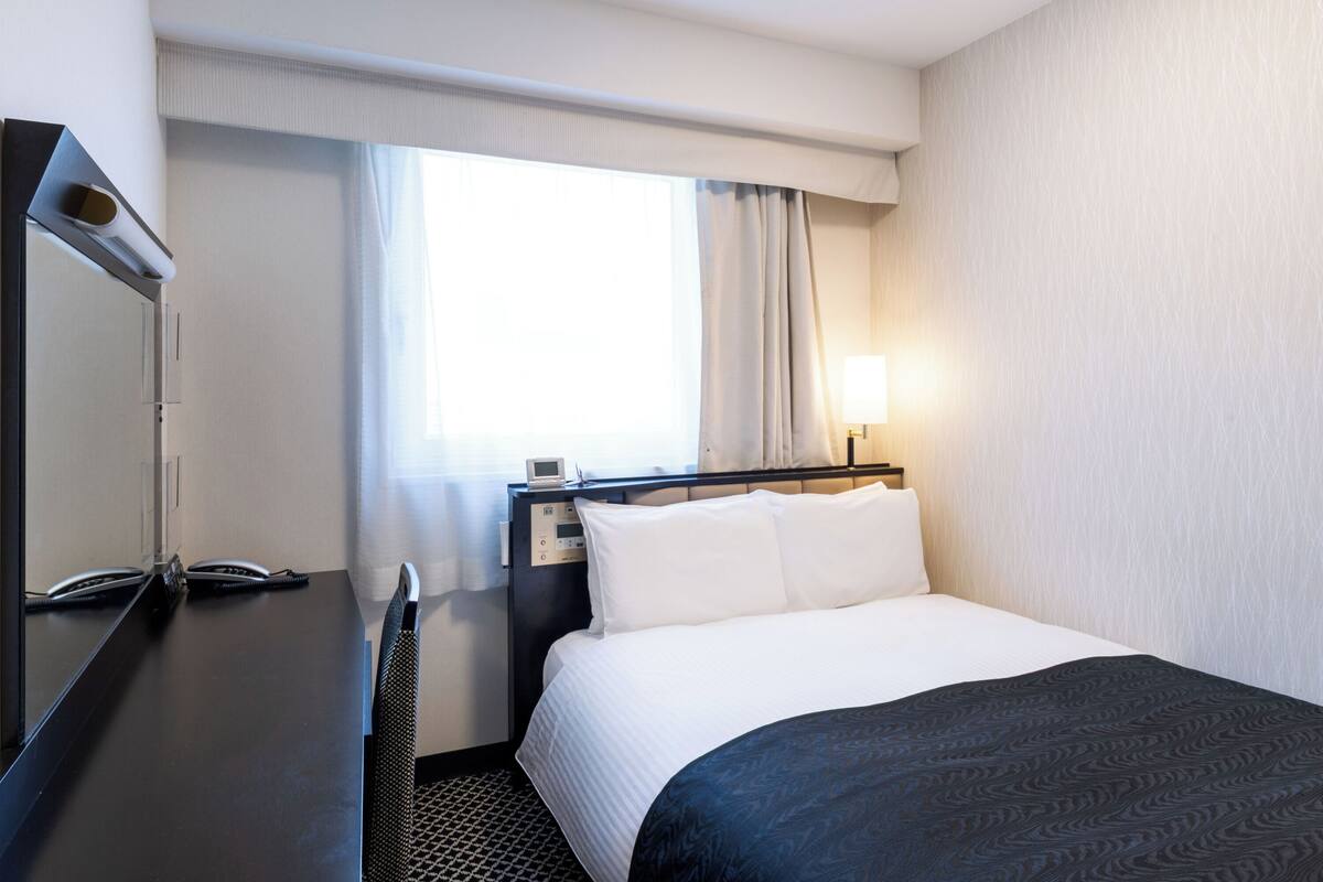 Une chambre d’hôtel avec un lit, une table de chevet, une lampe et une fenêtre avec des rideaux.