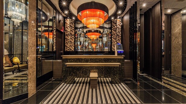 A modern lobby with a central reception desk, large chandeliers, and a striped carpet.