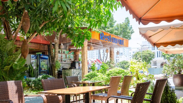 An outdoor cafe with wicker furniture and a restaurant sign. - Ariel Homes Boutique Hotel (Da Nang)
