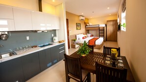 A compact hotel room with a kitchenette, a bed with a wooden headboard, and a dining area with a table and chairs. - Ariel Homes Boutique Hotel (Da Nang)