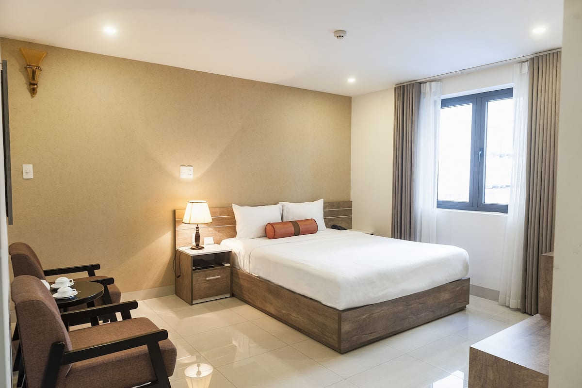 Ein Hotelzimmer mit einem großen Bett, einem Nachttisch mit Lampe, einem Sessel und einem kleinen Tisch mit Tassen.