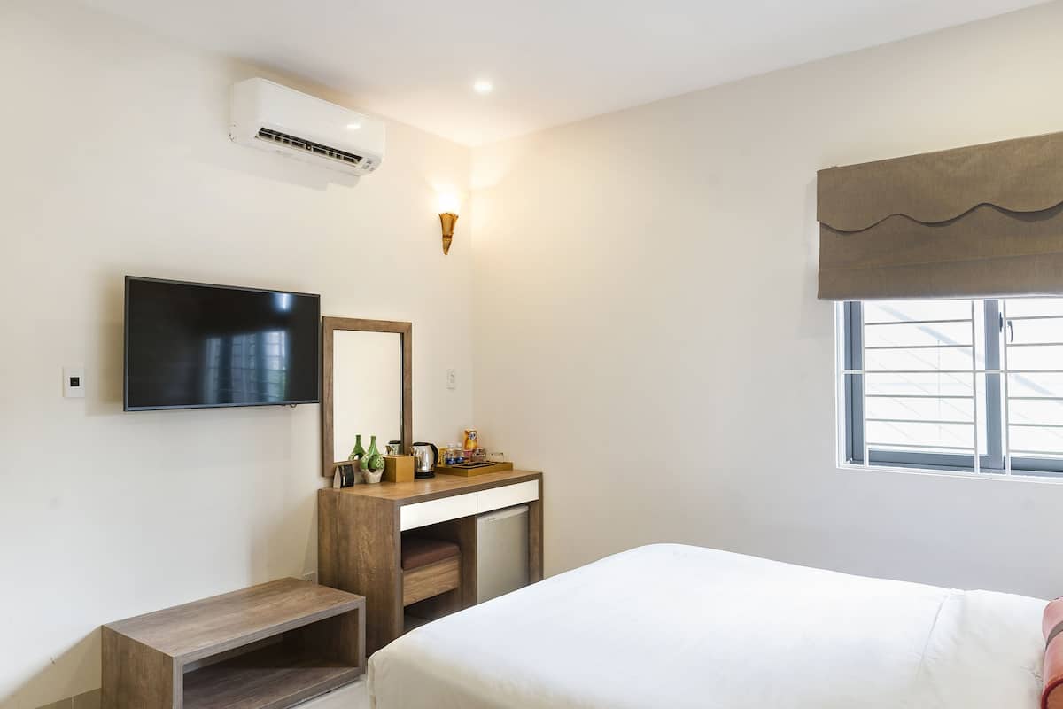 Ein Hotelzimmer mit Bett, Wand-Fernseher, Schreibtisch mit Spiegel, kleines Regal und Fenster mit Vorhang.