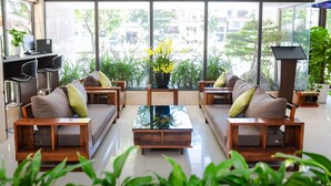 A modern living room with a sofa set, a coffee table, and a large window offering a view of greenery and buildings. - Ariel Homes Boutique Hotel (Da Nang)