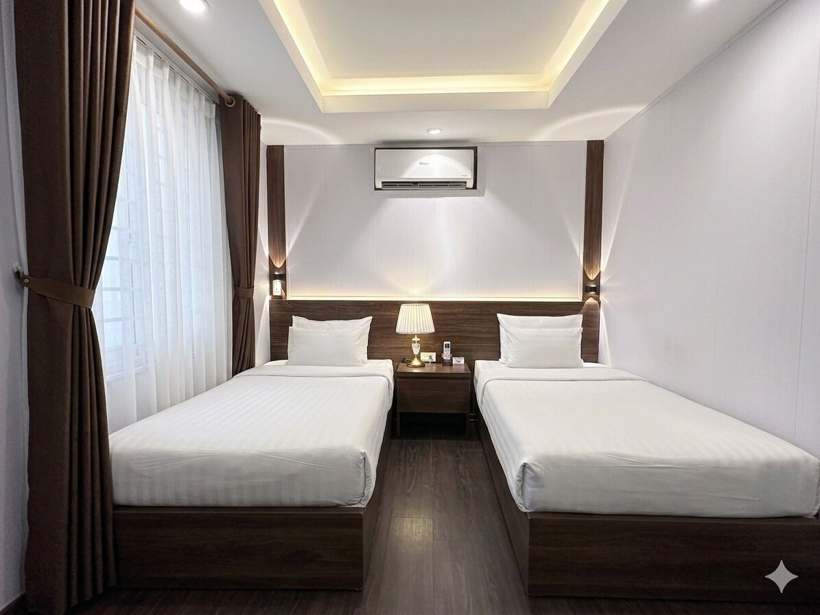 A hotel room with two beds, a bedside table with a lamp, an air conditioning unit, and a ceiling light.