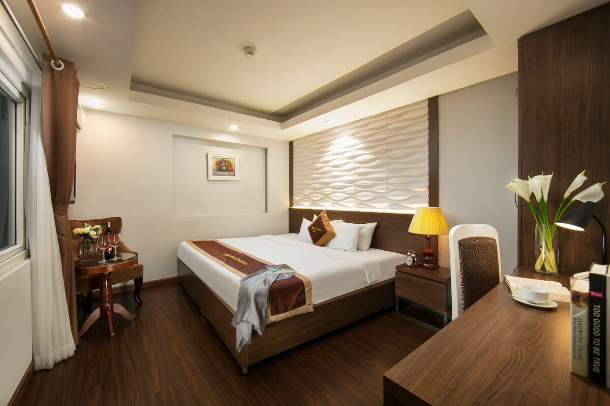 Een hotelkamer met een houten bed, een bureau met een lamp, een stoel en een nachtkastje met een klok.