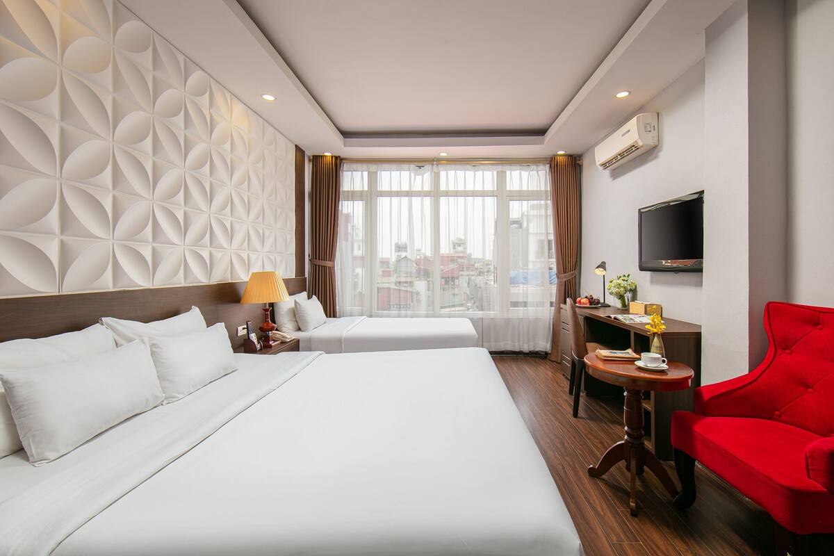 Een hotelkamer met twee bedden, een bureau, een rode stoel, een televisie en uitzicht op de stad.