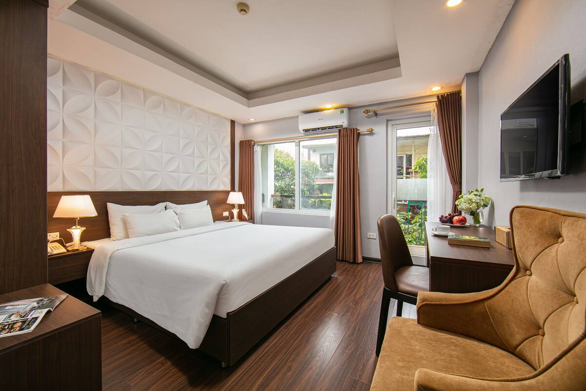 Een hotelkamer met een groot bed, een bureau met stoel, een televisie en een raam met gordijnen.