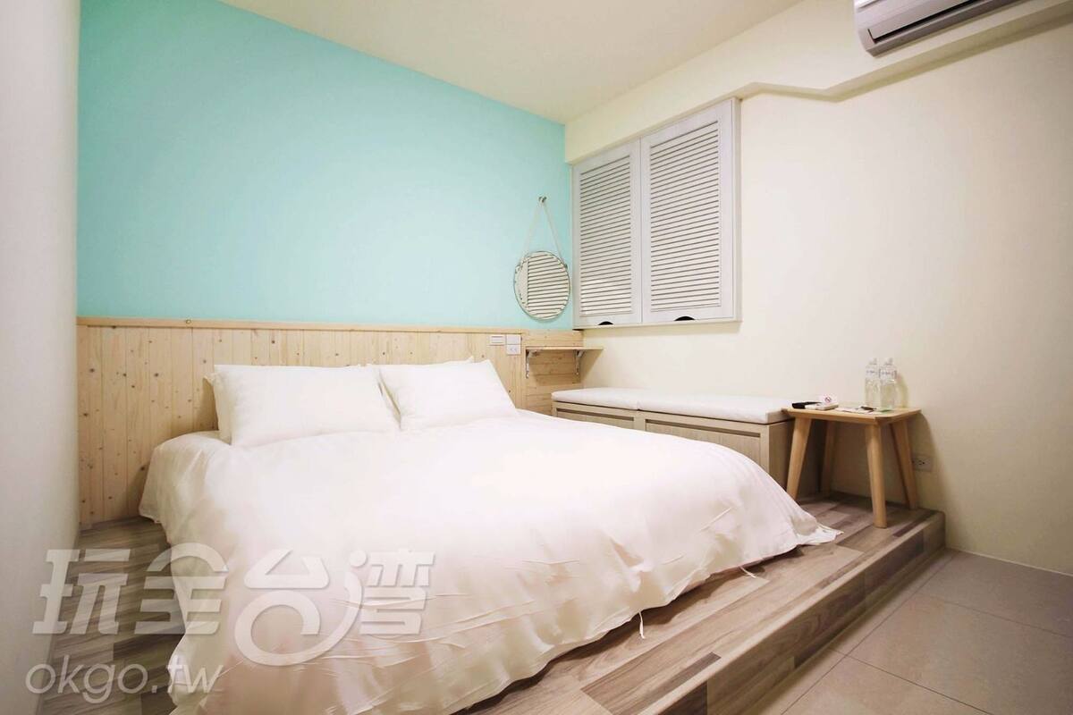 Une chambre à coucher comprenant un lit, une table de chevet, une fenêtre avec des volets et un appareil de climatisation.