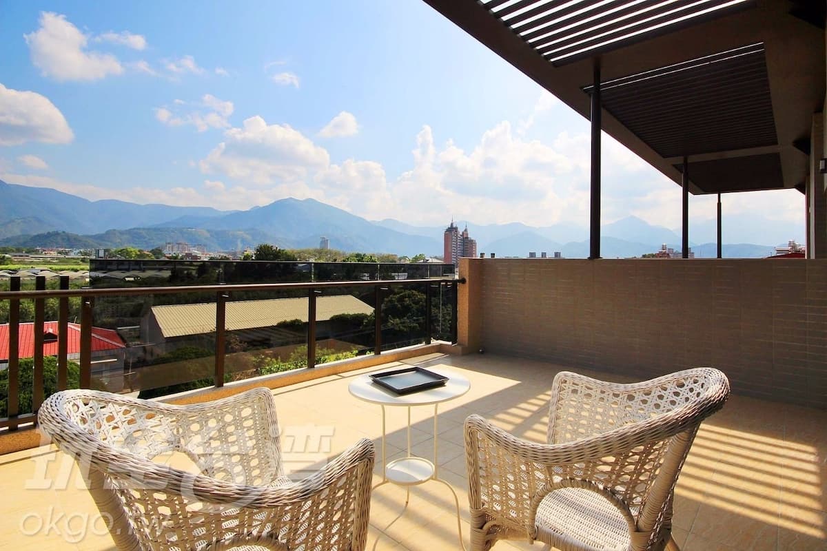 Un balcon avec des fauteuils et une table en osier, offrant une vue sur le paysage urbain et les montagnes.