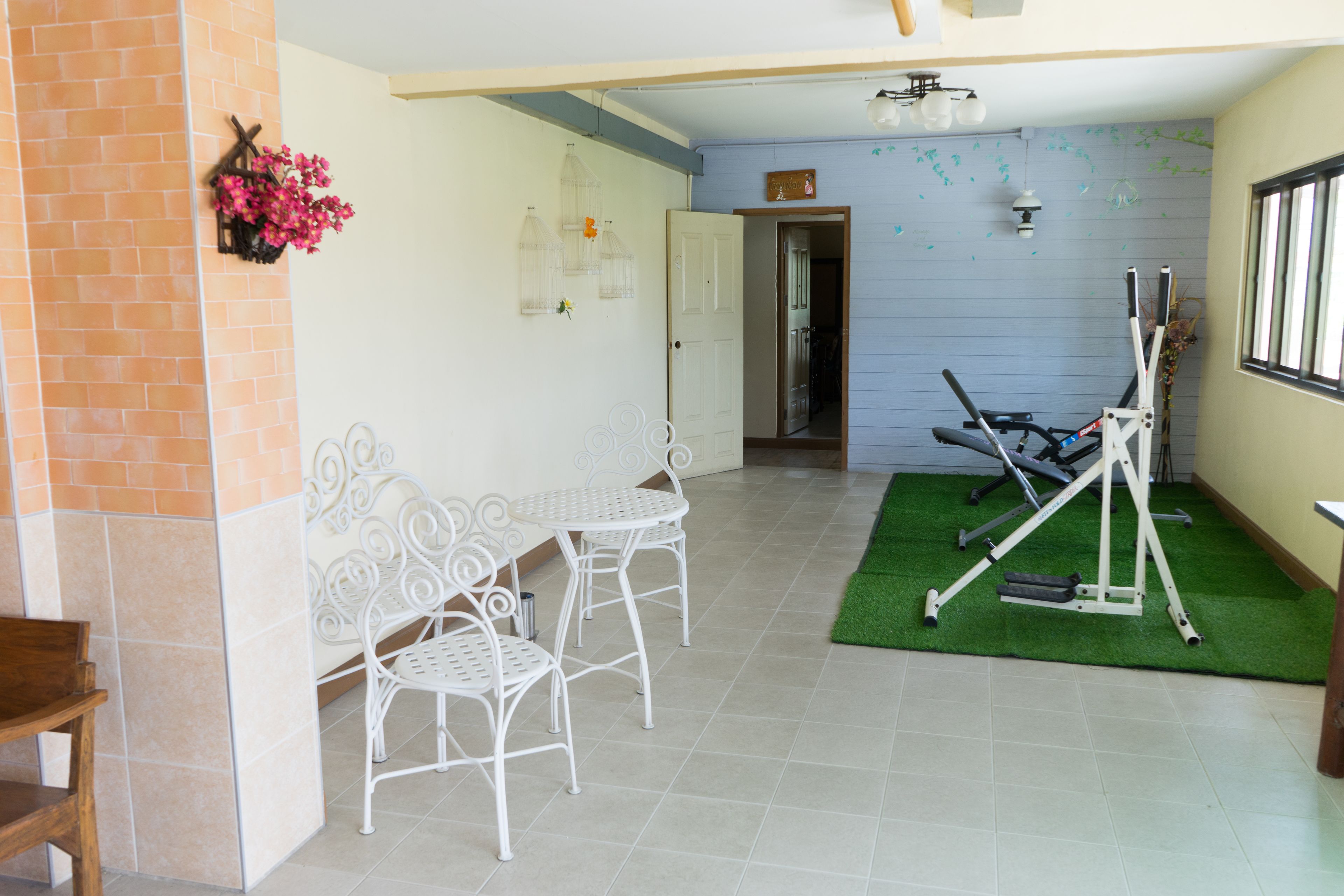 Una habitación con pared de ladrillo, una mesa y sillas de metal blanco, una colchoneta de ejercicios verde y una cinta de correr.