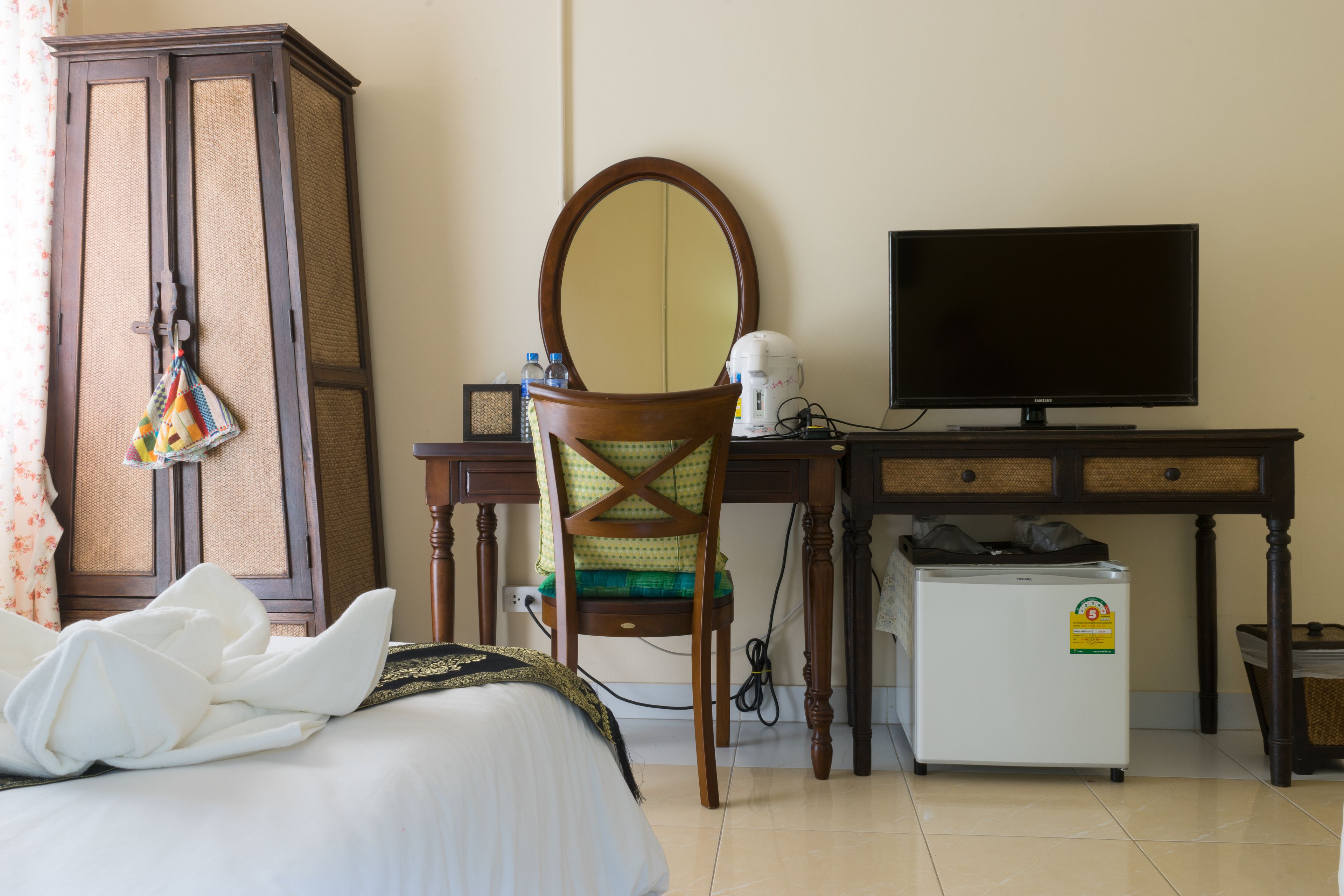 A hotel room with a bed, a desk with a television, a wardrobe, and a small refrigerator.