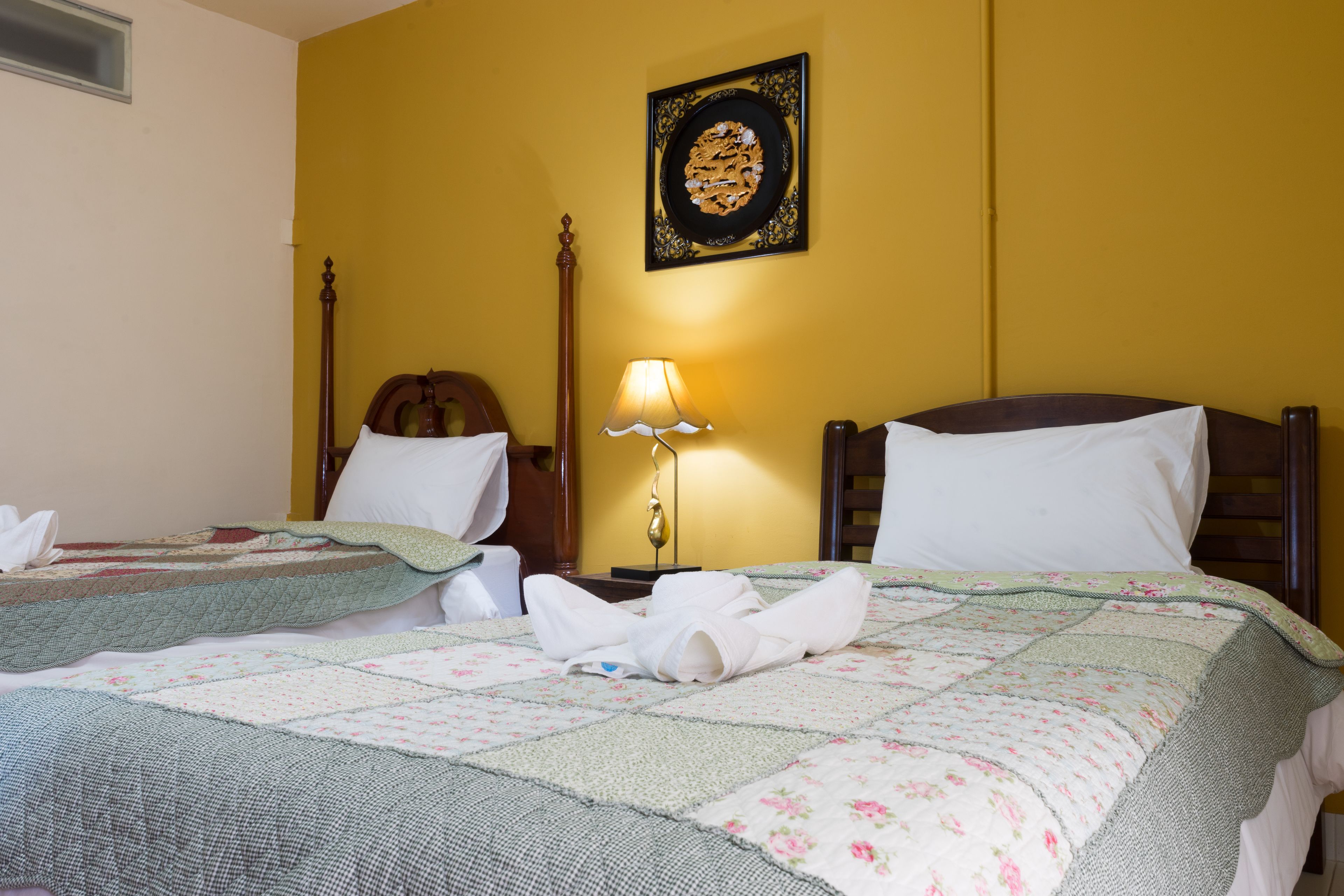 A hotel room with two beds, a wooden headboard, a bedside lamp, and a wall-mounted artwork.