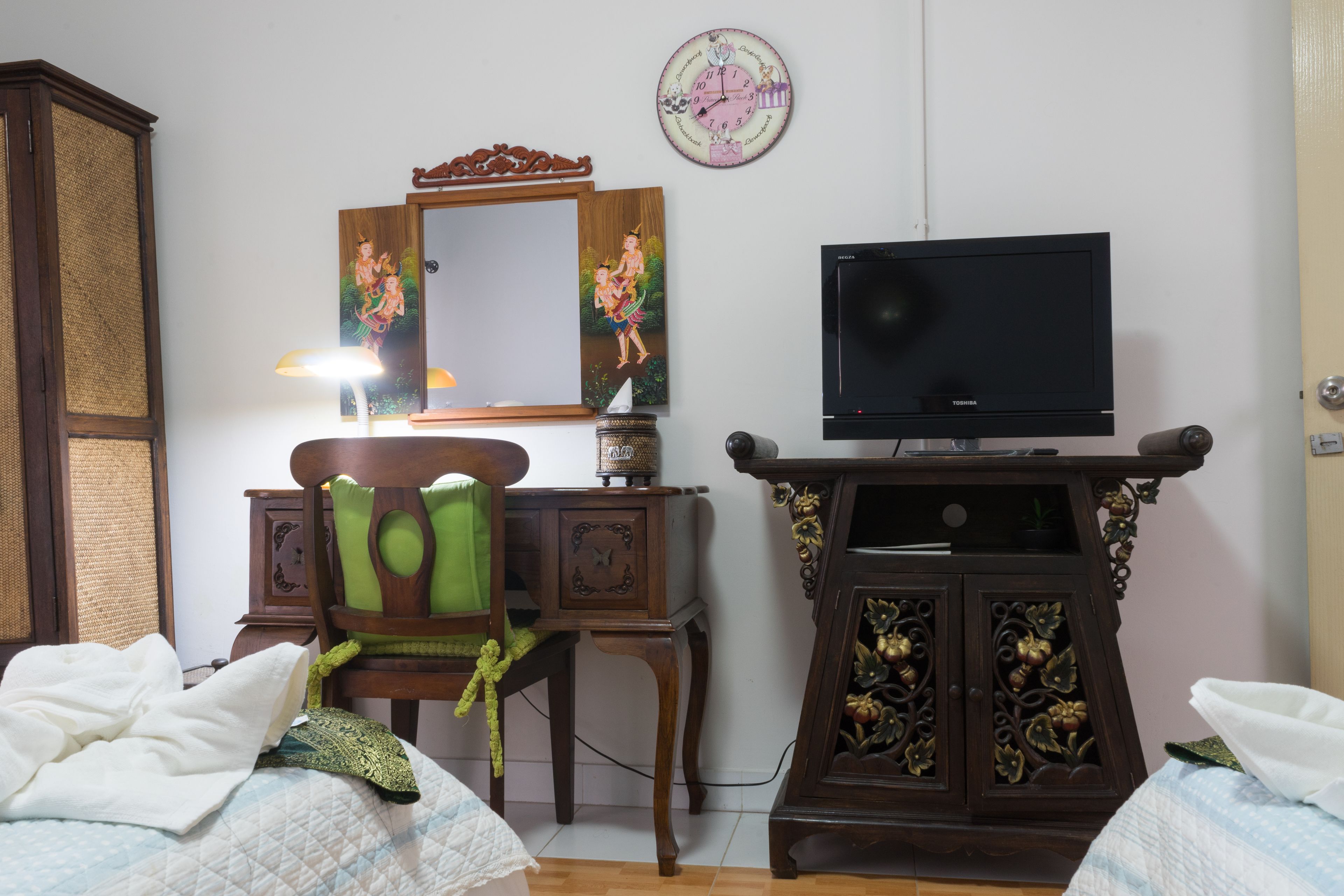 A bedroom with a bed, a desk with a lamp, a television, and a cabinet.