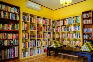 A library with multiple bookshelves filled with books, a bench with cushions, and an air conditioning unit on the wall. - Taratai Villa (Pattaya)