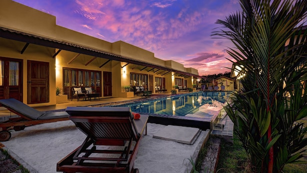 A poolside area with lounge chairs and a swimming pool, surrounded by a building with multiple windows and a covered patio. - Taratai Villa (Pattaya)