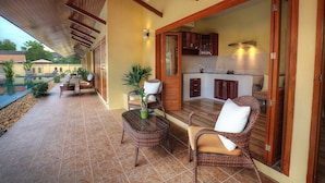 A covered outdoor area with wicker furniture, a pool, and a kitchen visible through an open door. - Taratai Villa (Pattaya)