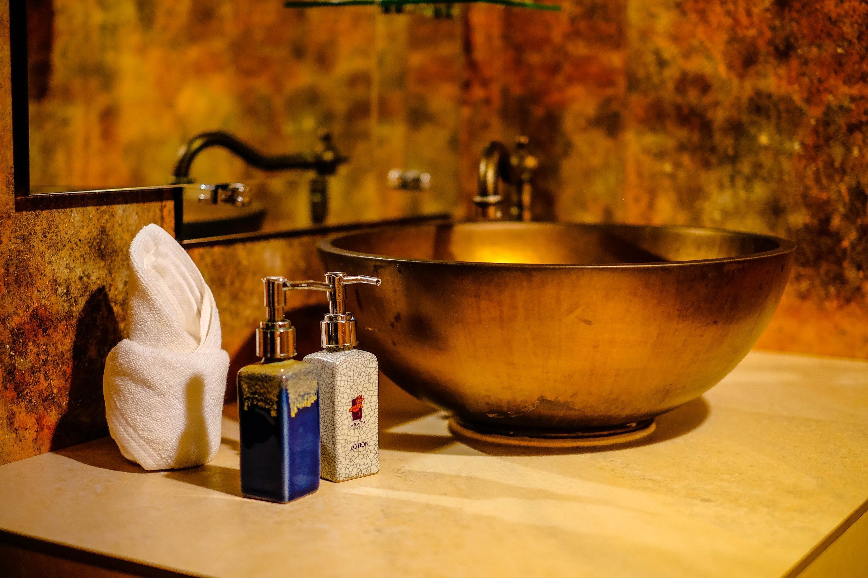 Une salle de bain avec un grand lavabo en laiton, une serviette et deux distributeurs de savon.
