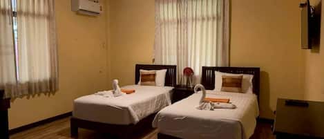 A hotel room with two beds, a wooden floor, an air conditioning unit, and a television on a stand.