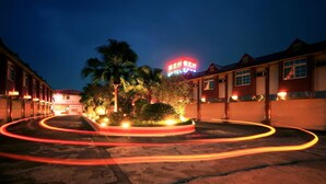 A hotel with a neon sign, palm trees, and a circular light trail. - Cherry Blossom Motel (Puli)