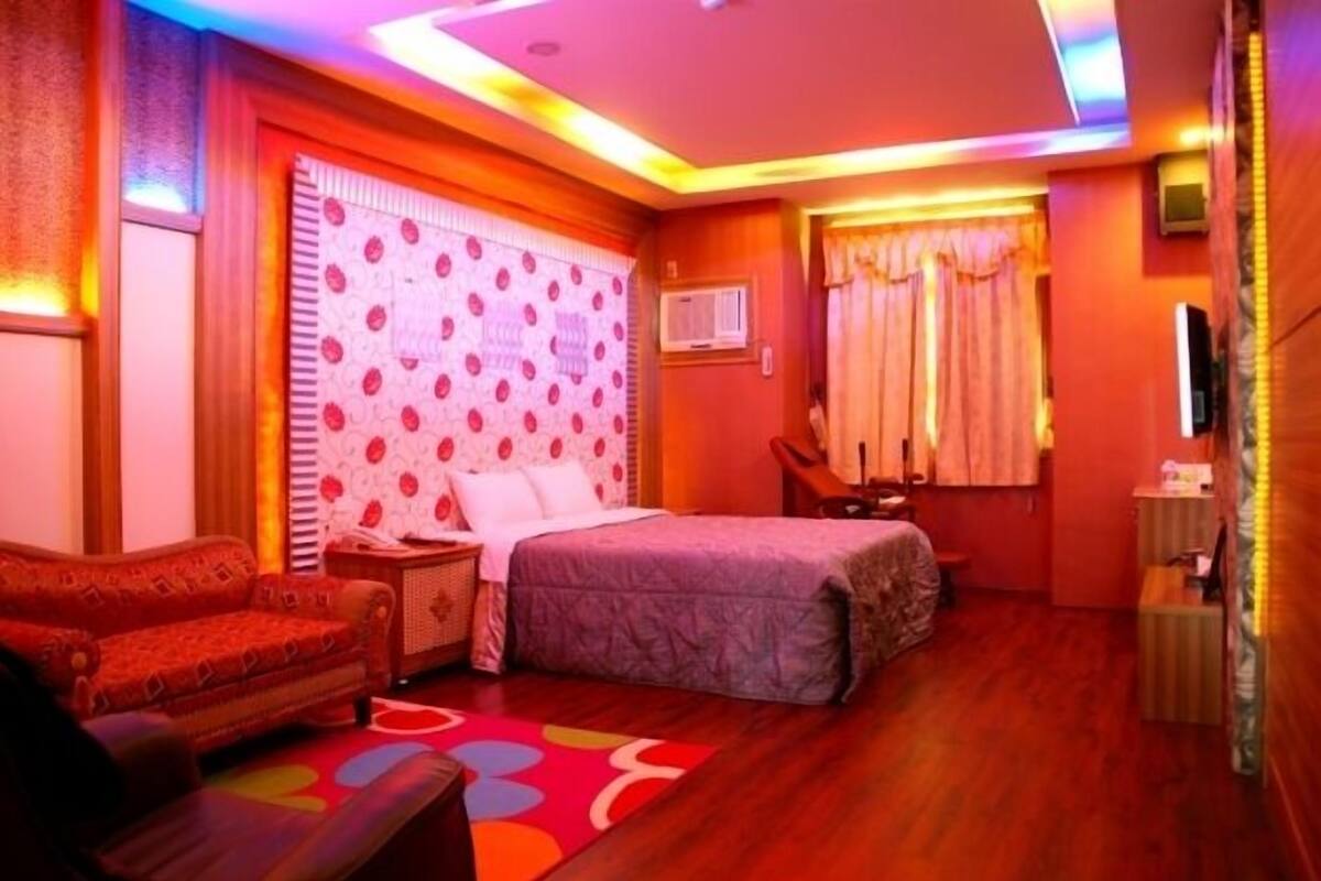 A bedroom with a bed, a sofa, a bedside table, and a window with curtains.