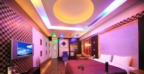 A hotel room with a checkered wall pattern, a bed, a TV, and a ceiling with colorful lighting. - Cherry Blossom Motel (Puli)