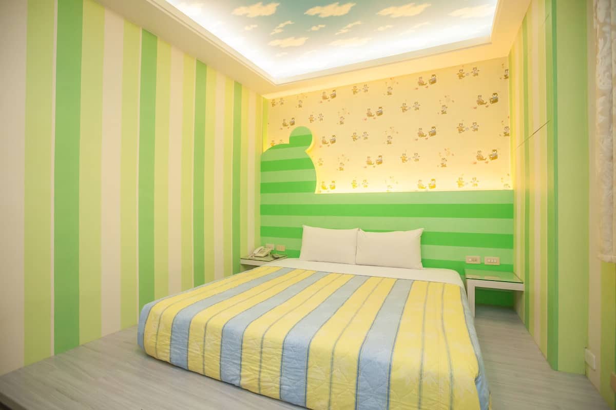 A bedroom with a striped green and white wall, a bed with a striped yellow and blue bedspread, a nightstand with a telephone, and a ceiling with a cloud design.