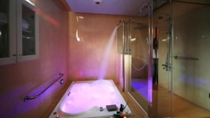A spa room with a hot tub, a glass shower enclosure, and a wooden floor. - Cherry Blossom Motel (Puli)