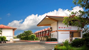 A hotel with a red roof and white walls, named Cherry Blossom Motel, with a parking area and greenery around. - Cherry Blossom Motel (Puli)