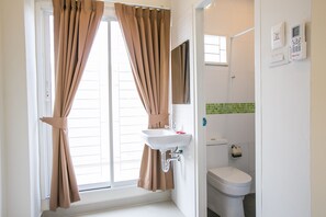 A bathroom with a white sink, a toilet, and a window with curtains. - J-House Phetchaburi (Phetchaburi)