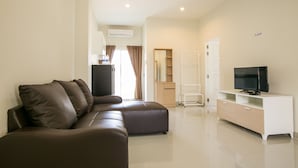 A modern living room with a brown sectional sofa, a white TV stand, and a large mirror. - J-House Phetchaburi (Phetchaburi)