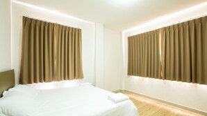 A hotel room with a bed, curtains, and a nightstand. - J-House Phetchaburi (Phetchaburi)