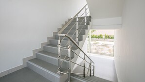A modern staircase with metal railings and a view of a balcony with outdoor furniture. - J-House Phetchaburi (Phetchaburi)