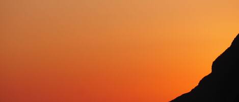 A sunset over a coastal landscape with prominent rock formations silhouetted against the sky.