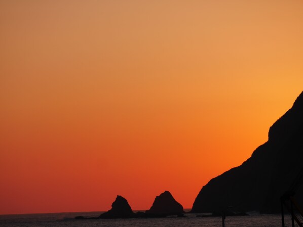 A sunset over a coastal landscape with prominent rock formations silhouetted against the sky.