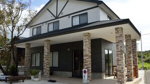 A two-story building with a covered porch supported by stone pillars, large windows, and a sign indicating no parking. - Lodge Ocean (Hachijo)