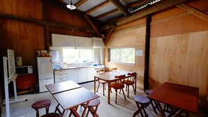 A wooden interior with a kitchen area, dining tables, and chairs. - Lodge Ocean (Hachijo)