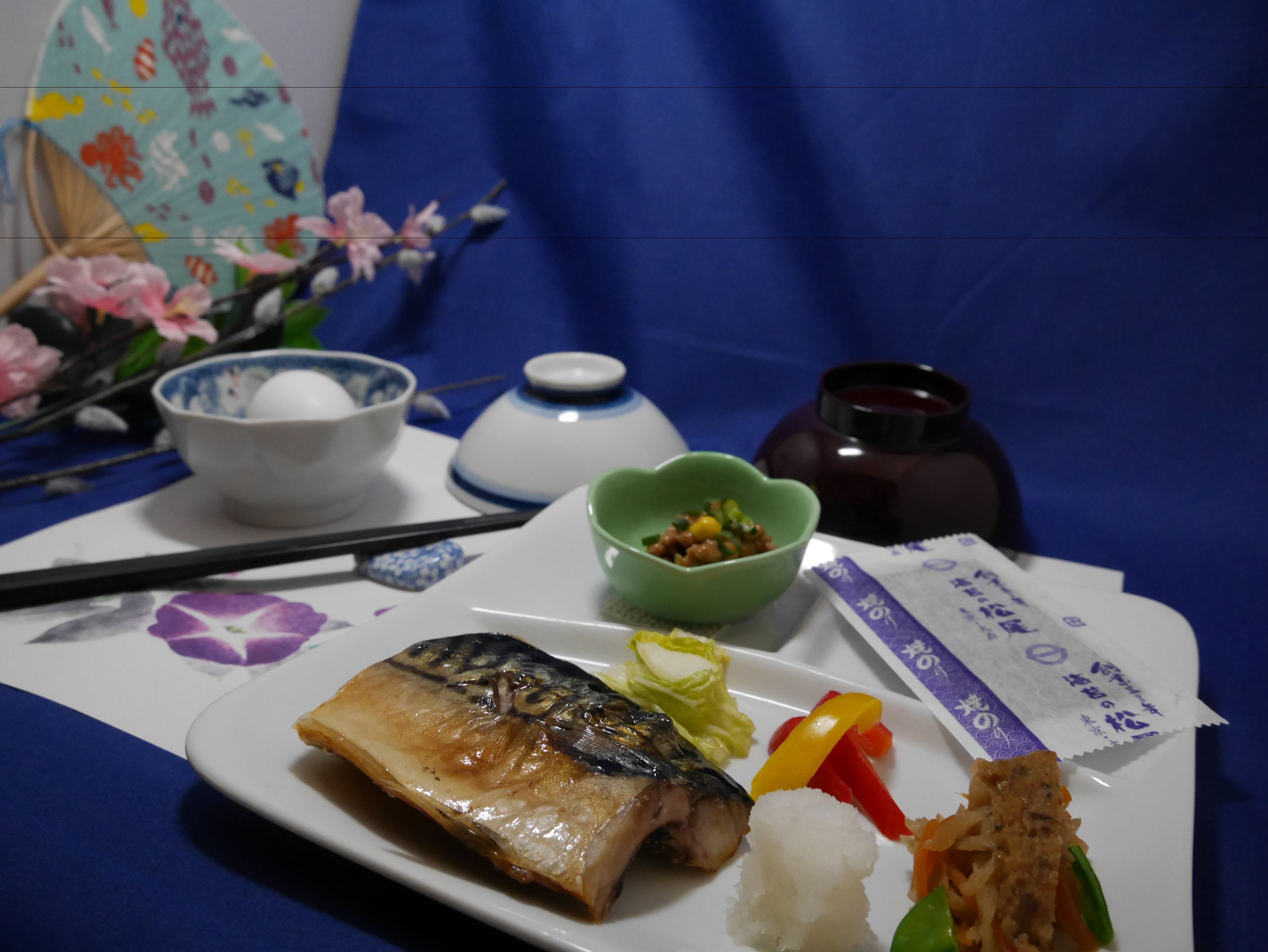 Un plato con pescado, arroz, verduras y un bol verde de comida sobre una mesa con palillos, una taza y un adorno.