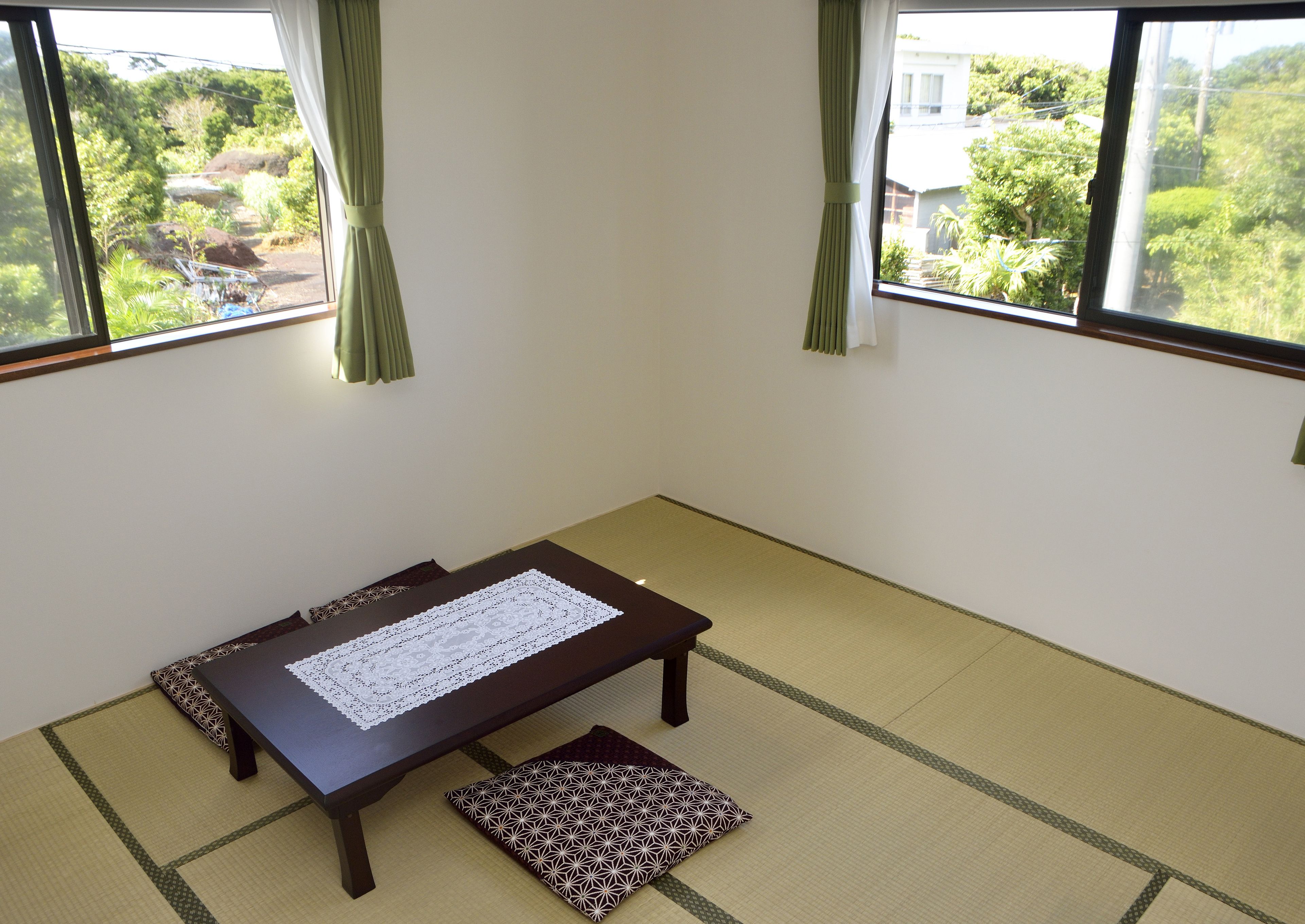 A tatami mat room with a low table, cushions, and a view of greenery outside.