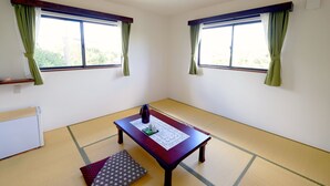 A room with tatami flooring, a low table with a mat, two windows with green curtains, and a radiator. - Lodge Ocean (Hachijo)