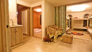 A room with a wooden cabinet, a bed with a patterned blanket, a small wooden stool, and a bunk bed with toys. - Moonlight Pension (Seogwipo)
