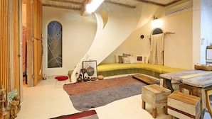 A cozy loft-style room with a curved ceiling, a yellow sofa, wooden furniture, and a large window with a decorative glass design. - Moonlight Pension (Seogwipo)