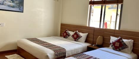 A hotel room with two beds, a wooden headboard, a window with blinds, a wall-mounted picture, and a small rug.
