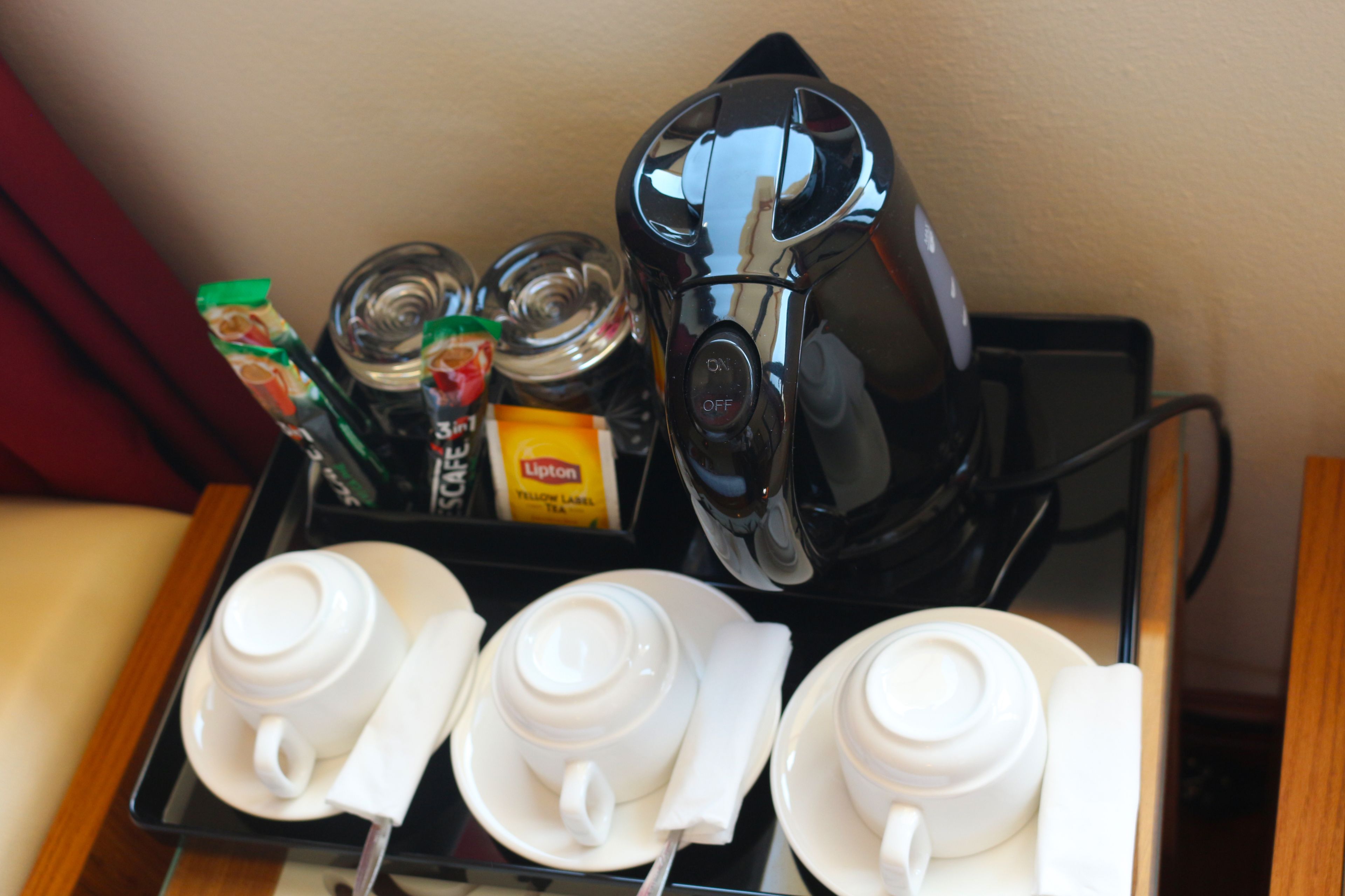 Una bandeja con una cafetera, té Lipton y tres tazas blancas con sus platillos.