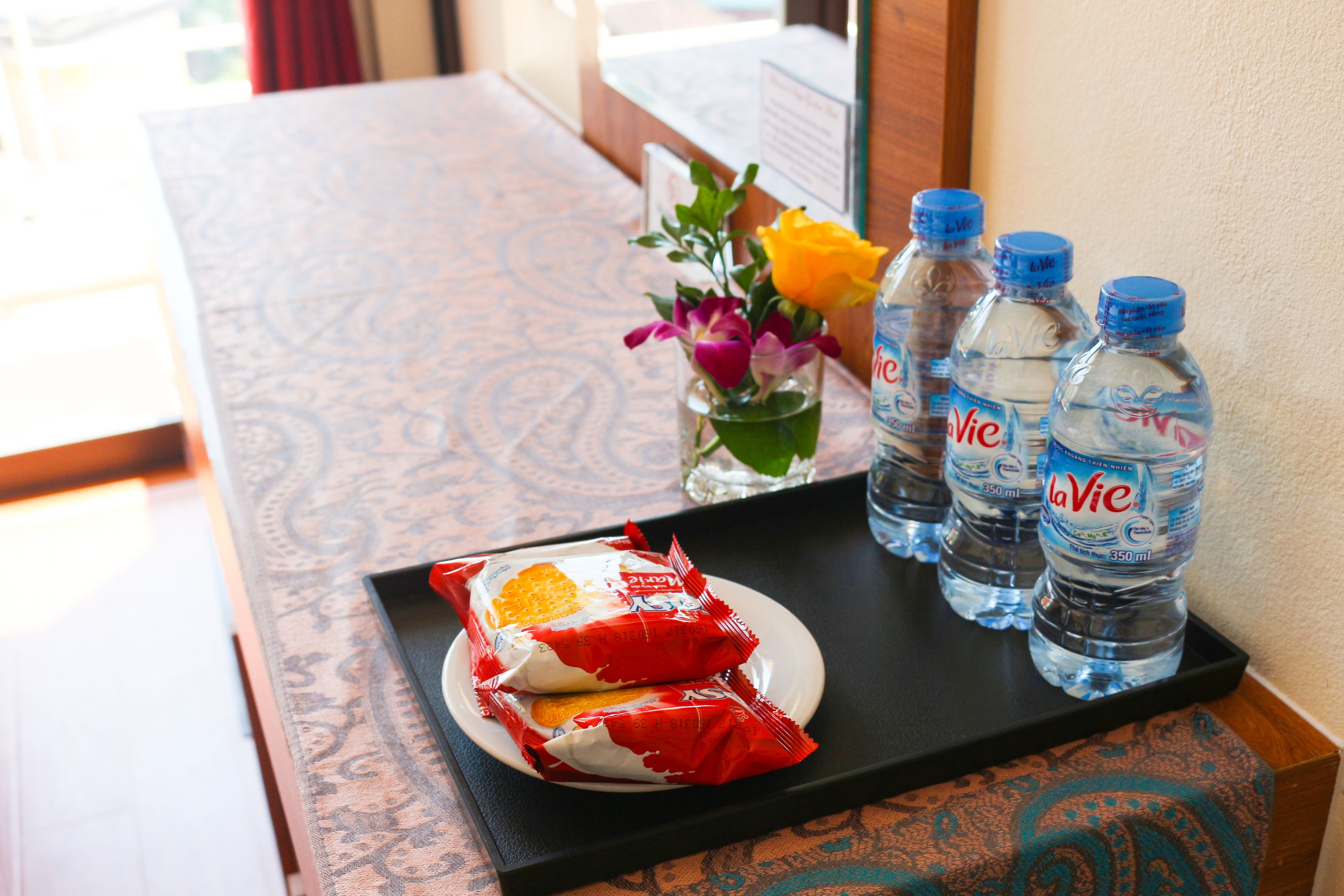 Un plateau contenant des aliments emballés, des bouteilles d’eau et un vase avec des fleurs, posé sur une table.