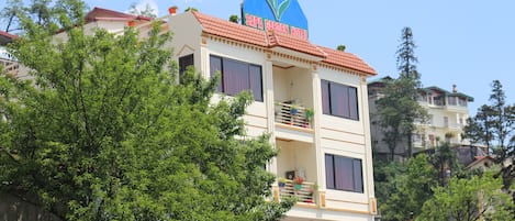Un hotel de varios pisos con un letrero llamativo en el techo, balcones con plantas en macetas y una cerca blanca de piquete.